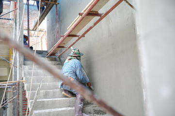Group of workers stand on the steel scaffolding and builds plastered cement wall in the house under construction
