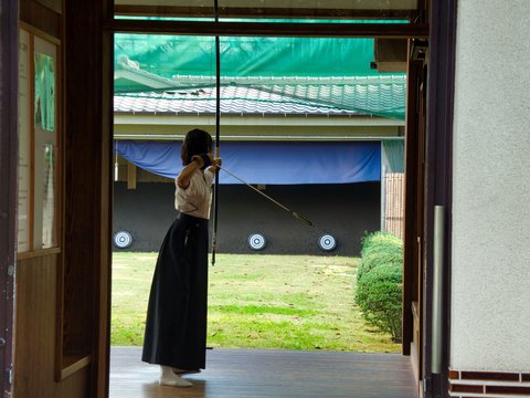 Girl holding bow and arrow and aiming at a target in a garden