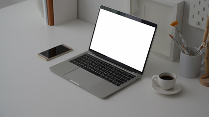 Cropped shot of workspace with blank screen laptop, office supplies, decorations and red coffee cup on white desk