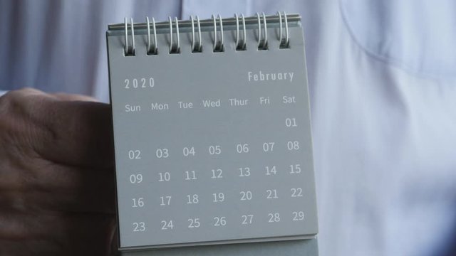 A Man's Hand Flips The Sheets Of A 2020 Year Black Mini Monthly Standing Desk Calendar From January To February Month.