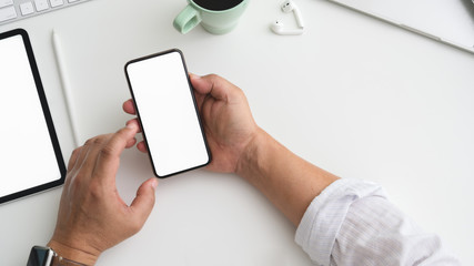 Overhead shot of businessman working on smartphone in trendy workspace with other office supplies on white desk
