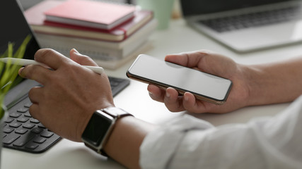 Fototapeta premium Side view of businessman working on smartphone in modern workspace with digital tablet, laptop and office supplies