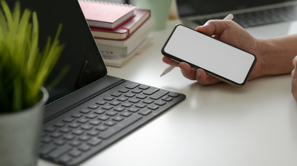 Cropped shot of businessman holding smartphone in modern workspace with digital tablet and office supplies