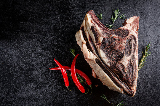 Modern kitchen. Dry aged beef, veal meat with red pepper and rosemary lies on a black background. board background image, copy space text, top view
