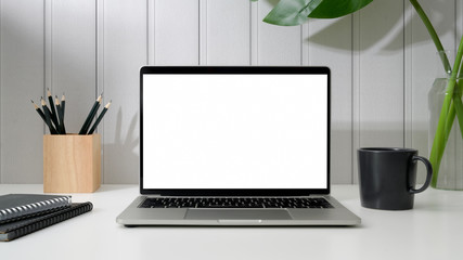 Fototapeta premium Cropped shot of workspace with open blank screen laptop, office supplies and coffee cup on white table with white plank wall