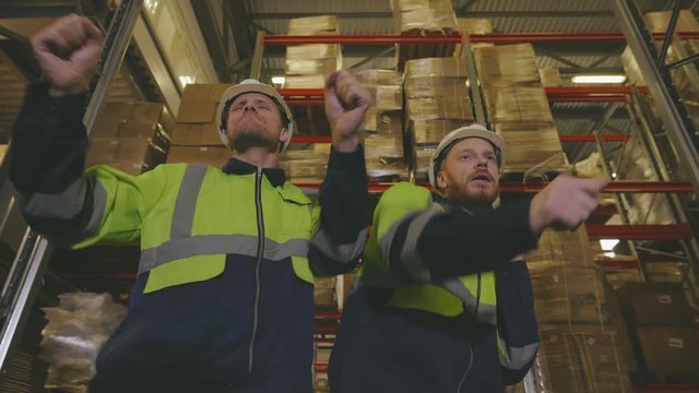 Low angle view of two warehouse workers happily dancing in warehouse