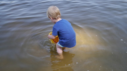 Dziecko bawi się w wodzie. Chłopiec bawi się wiaderkiem i stoi w wodzie. © Marcin