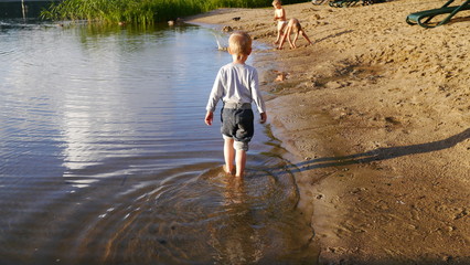 Dziecko bawi się w wodzie. Chłopiec bawi się wiaderkiem i stoi w wodzie.