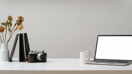 Cropped shot of workspace with laptop, camera, coffee up, office supplies and dry roasts vase on white wooden table