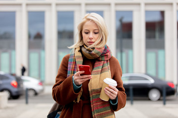 Beautiful blonde woman with cup of coffee using mobile phone