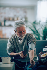 Old man measuring blood pressure. Sad senior man in living room. 