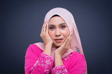 Headshot portrait of a beautiful female Muslim model wearing pink kurung with hijab, a modern urban lifestyle apparel for Muslim women isolated on grey background. Beauty and hijab fashion concept.