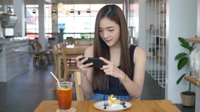 4K Beautiful Asian girl taking photo of delicious cake at coffee shop, Smartphone or mobile phone photography hobby in new lifestyle