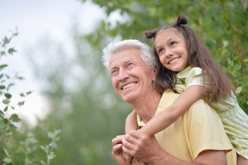 Happy grandfather and granddaughter having fun in park