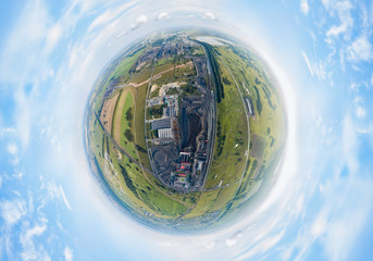 Aerial panoramic 360 degree view like a little earth planet of a large plant with mines for the extraction of coal. Mounds of black coal near production and industry under blue sky with clouds.