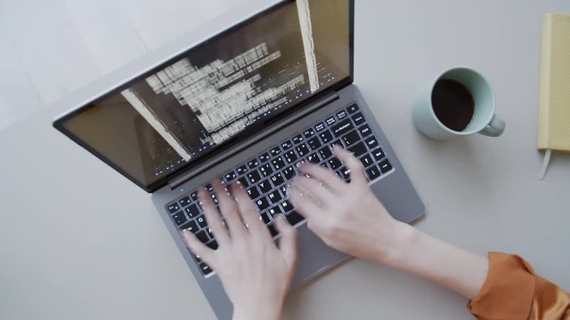 Timelapse top shot of hands of anonymous female programmer sitting and working at desk in office, typing computer code on laptop keyboard, and lines of digital symbols running on screen