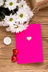 A pink notebook on a wooden table next to flowers, coffee bars and a gift. The concept of the first school anniversary for Valentine's Day