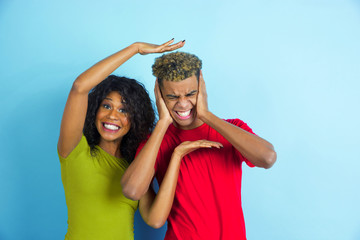 Having fun and gremaces. Young emotional african-american man and woman in casual clothes posing on blue background. Beautiful couple. Concept of human emotions, facial expession, relations, ad.