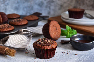 Chocolate muffins with chocolate moss sauce and mint on a concrete background.