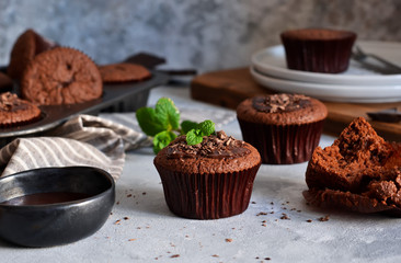 Chocolate muffins with chocolate moss sauce and mint on a concrete background.