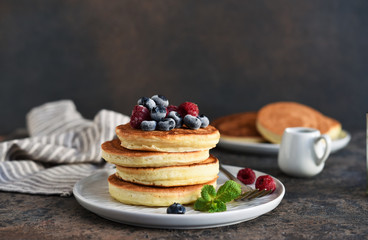 Beautiful pancakes with berries and sauce on a dark concrete background.