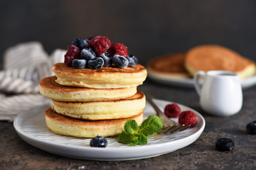 Beautiful pancakes with berries and sauce on a dark concrete background.