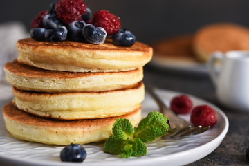 Beautiful pancakes with berries and sauce on a dark concrete background.