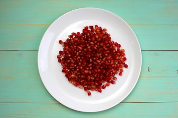 A bunch of red pomegranate seeds lie on a white plate