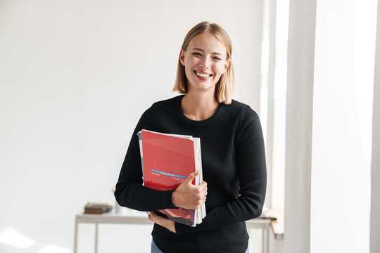 Blonde woman student indoors holding copybooks.