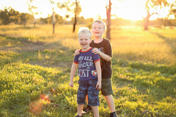 Little boy giving his little brother a piggy back. Boys playing together in vibrant field at sunset with copy space.