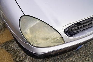 Close up hazy yellowed dirty car unpolished cloudy foggy front plastic automobile headlight worn