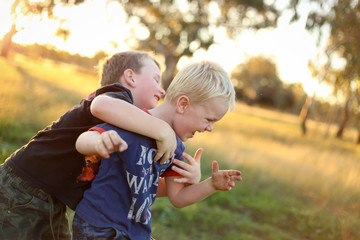 Fototapeta premium Little boy giving his little brother a piggy back. Boys playing together in vibrant field at sunset with copy space.