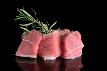 Pieces of raw uncooked fresh meat with rosemary isolated on black background, front view, macrophoto