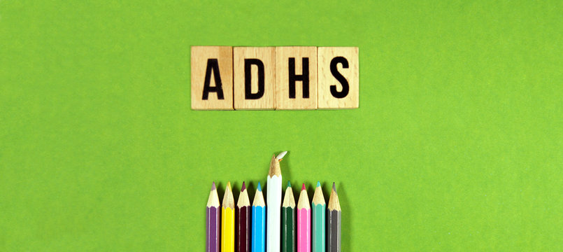 panoramic view of the german word ADHS Aufmerksamkeits-defizit- Hyperaktivit&auml;ts-syndrom on wooden blocks with multicolored pencils on green background. ADHS, german for ADHD concept