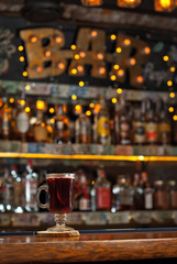 Red cocktail on bar counter. Drink with wine, fruit and cinnamon on the background of bottles with alcohol. Glass with booze on a wooden board.