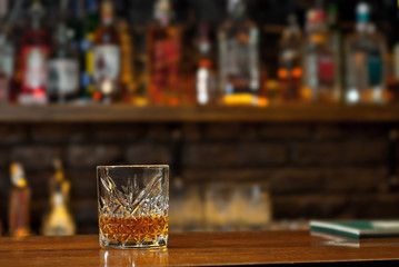 Yellow cocktail on bar counter. Whiskey, rum or brandy on the background of bottles with alcohol. Glass with booze on a wooden board.