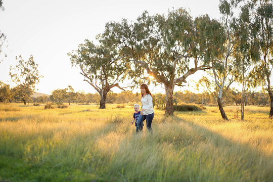Mother and son playing together in a picturesque field with long grass at sunset. Family time. Mother-son bond. Beautiful image for mother's day with copy space.