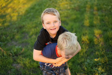 Two young brothers hugging with faces pressed together. Little boy with missing teeth. Children playing at golden hour.