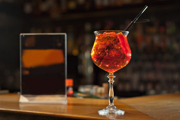 Red cocktail on bar counter. Drink with martini, gin, rum, tequila and fruit on the background of bottles with alcohol. Glass with booze on a wooden board.