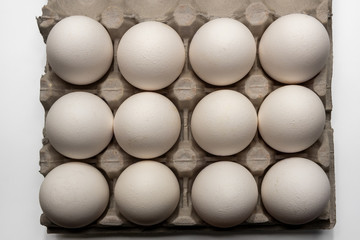 A dozen chicken eggs in a cardboard box on a white background. Isolated top view.