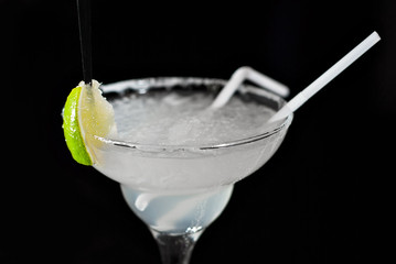 White cocktail on bar counter. Drink with martini, gin, tequila and lime. Glass with booze on black...