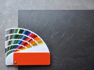 Color palette guide, fan, catalogue on grey and black background. Ral color fan  with orange cover on conсrete texture