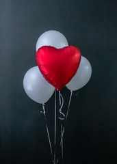 Fototapeta na wymiar Red heart-shaped balloon and white round air balloons on a black background. Valentine's Day, holiday, love. Place for text, vertical photo.