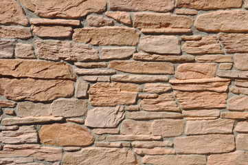 Texture of red  broken stone of different sizes. Facing natural stone building walls.  Architectural background laid out of beautiful stone with cement joints