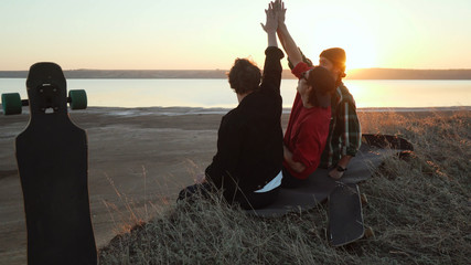 Friends give high five to each other sit at sea coast sunset