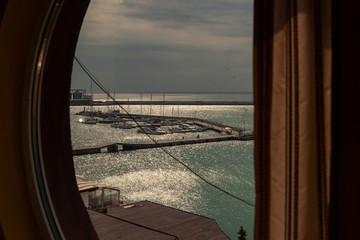 Room with a round window view over the docks with small boats on the coast of the Black Sea.