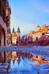 St Mary Tyn Church in Prague with reflection in a pool of water after Summer rain with tourists walking by towards Old Market Square in Prague