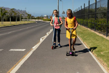 Caucasian schoolgirls riding push scooters