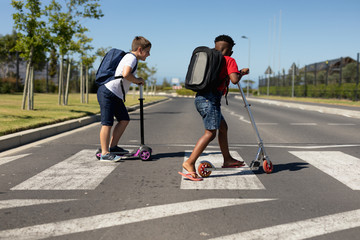 Schoolboys riding push scooters on a pedestrian crossing