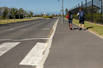 Schoolboys riding push scooters on the pavement